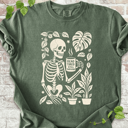 Dead Tired T-shirt on Comfort Colors™ Moss – shows a coffee-loving skeleton surrounded by botanical elements like mushrooms and Monstera leaves, printed in light ink