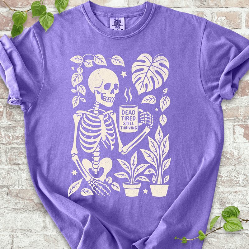 Dead Tired T-shirt on Comfort Colors™ Violet – features a skeleton holding coffee surrounded by Monstera leaves, mushrooms, and houseplants in a cozy goth design