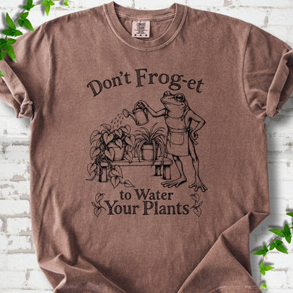 Espresso Comfort Colors® T-shirt laid flat, showing a frog in an apron watering potted plants, with “Don’t Frog-et to Water Your Plants” lettering.