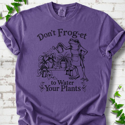 Grape Comfort Colors® T-shirt laid flat, showing a frog in an apron watering potted plants, with “Don’t Frog-et to Water Your Plants” lettering.