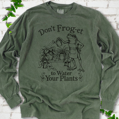 Hemp Comfort Colors® long sleeve T-shirt laid flat, showing a frog in an apron watering potted plants, with “Don’t Frog-et to Water Your Plants” lettering.