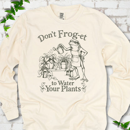 Ivory Comfort Colors® long sleeve T-shirt laid flat, showing a frog in an apron watering potted plants, with “Don’t Frog-et to Water Your Plants” lettering.