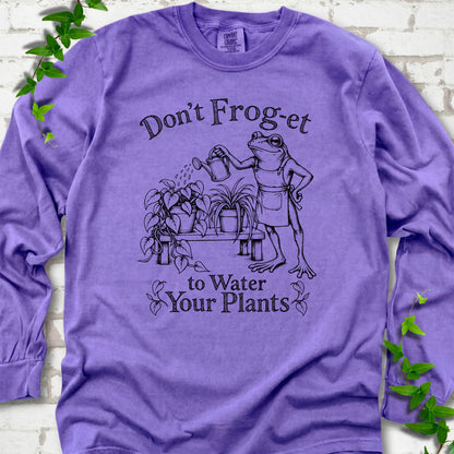Violet Comfort Colors® long sleeve T-shirt laid flat, showing a frog in an apron watering potted plants, with “Don’t Frog-et to Water Your Plants” lettering.