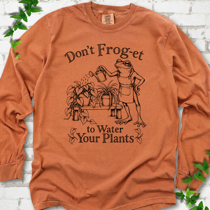 Yam Comfort Colors® long sleeve T-shirt laid flat, showing a frog in an apron watering potted plants, with “Don’t Frog-et to Water Your Plants” lettering.