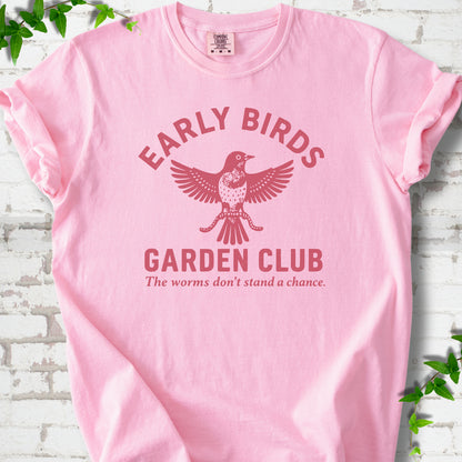 Blossom short sleeve T-shirt laid flat on white brick with greenery. Red bird holding worms between "Early Birds" and "Garden Club" chest lettering.