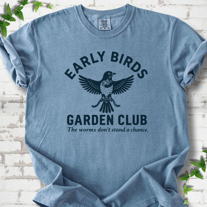 Blue Jean short sleeve T-shirt laid flat on white brick with greenery. Dark navy bird holding worms between "Early Birds" and "Garden Club" chest lettering.