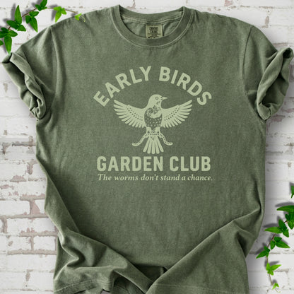 Moss short sleeve T-shirt laid flat on white brick with greenery. Pale green bird holding worms between "Early Birds" and "Garden Club" chest lettering.