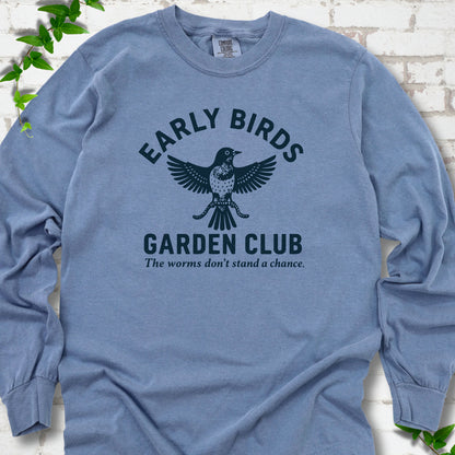 Blue Jean long sleeve T-shirt laid flat on white brick with greenery. Dark navy bird holding worms between "Early Birds" and "Garden Club" chest lettering.