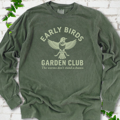 Hemp long sleeve T-shirt laid flat on white brick with greenery. Pale green bird holding worms between "Early Birds" and "Garden Club" chest lettering.