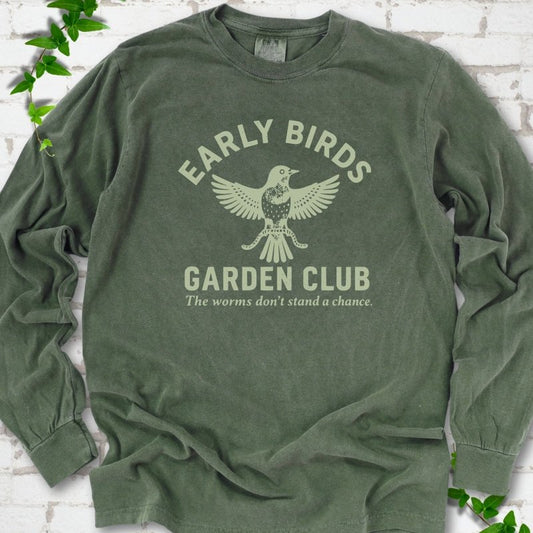 Hemp long sleeve T-shirt laid flat on white brick with greenery. Pale green bird holding worms between "Early Birds" and "Garden Club" chest lettering.