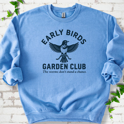 Carolina Blue crewneck sweatshirt laid flat on white brick with greenery. Dark navy bird holding worms between "Early Birds" and "Garden Club" chest lettering.