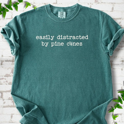 Blue Spruce Comfort Colors® T-shirt shown flat with "Easily Distracted by Pine Cones" text and a small pine cone graphic