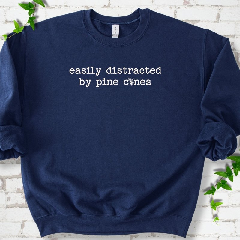 Navy classic sweatshirt shown flat with "Easily Distracted by Pine Cones" text and a small pine cone graphic