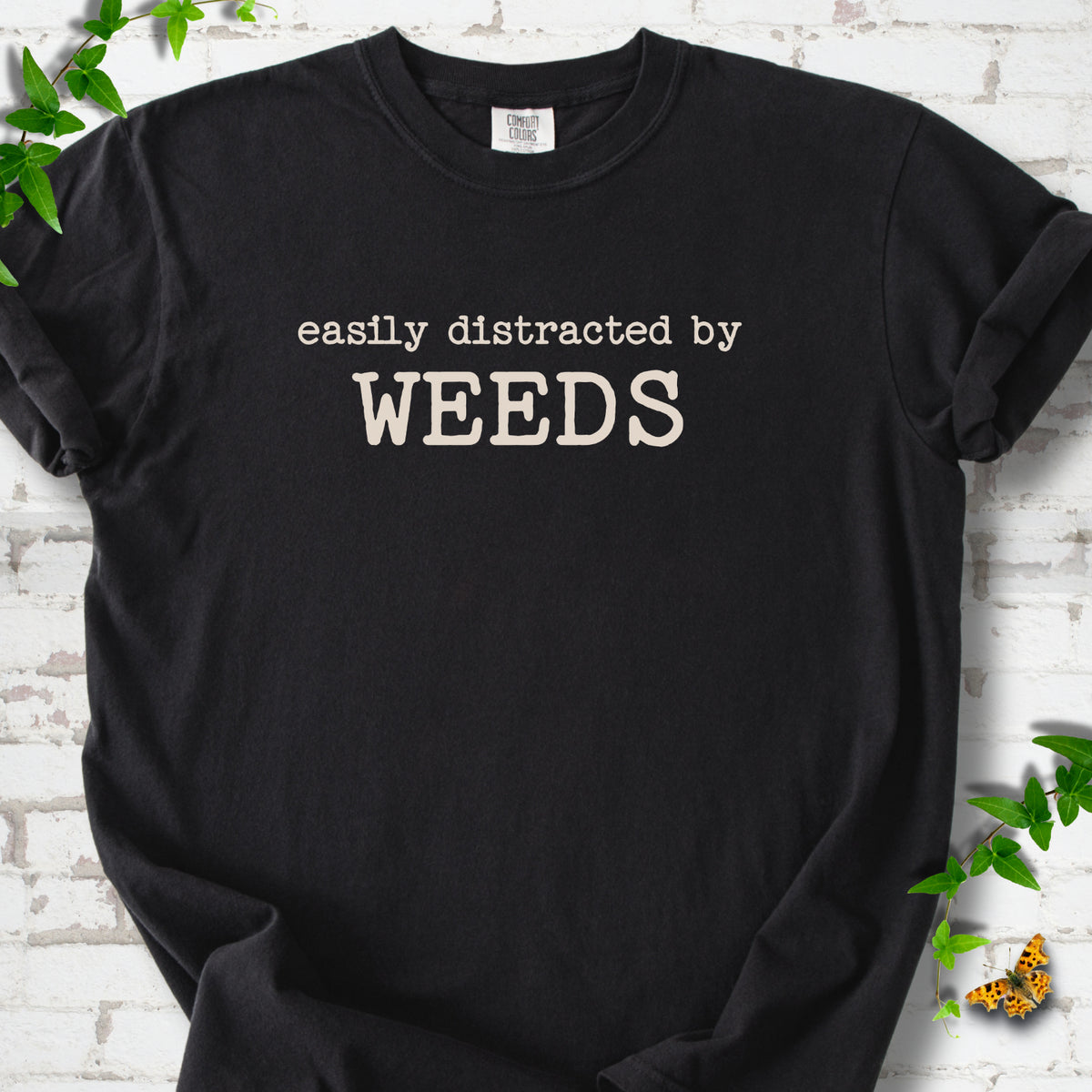Black Comfort Colors® T-shirt shown flat with cream "Easily Distracted by Weeds" gardening slogan
