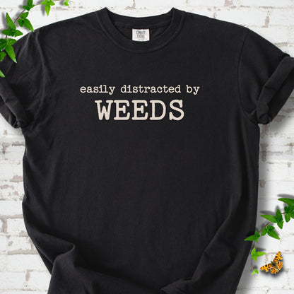 Black Comfort Colors® T-shirt shown flat with cream "Easily Distracted by Weeds" gardening slogan
