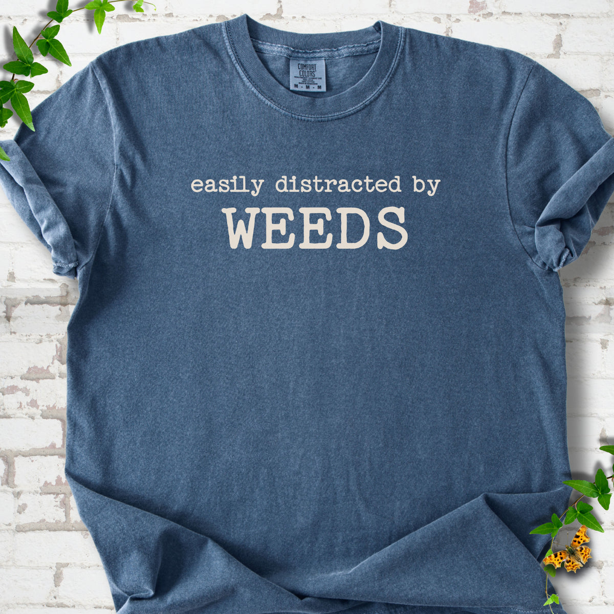 Denim Comfort Colors® T-shirt shown flat with cream "Easily Distracted by Weeds" gardening slogan