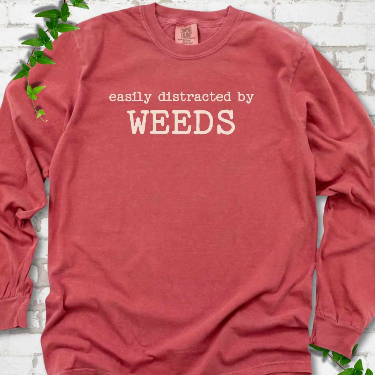 Crimson Comfort Colors® long sleeve T-shirt shown flat with cream "Easily Distracted by Weeds" gardening slogan