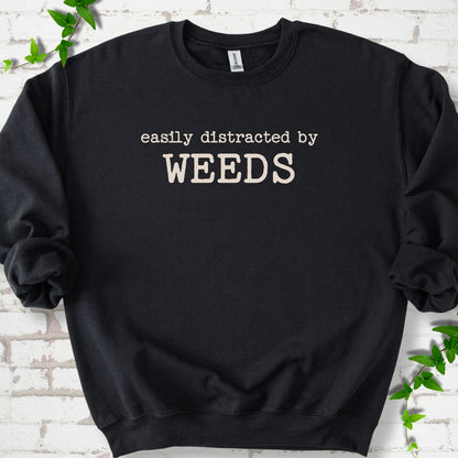 Black classic sweatshirt shown flat with cream "Easily Distracted by Weeds" gardening slogan