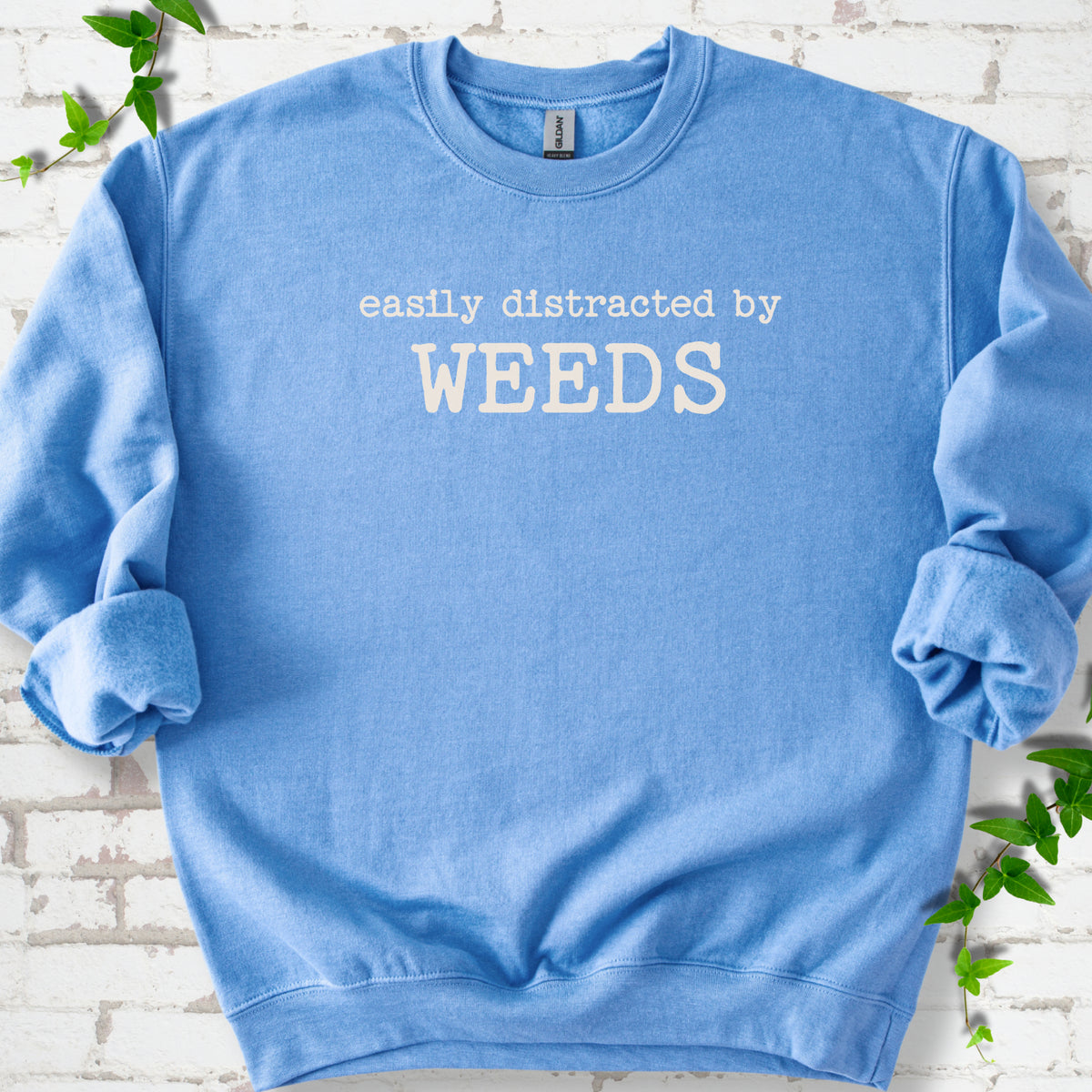 Carolina Blue classic sweatshirt shown flat with cream "Easily Distracted by Weeds" gardening slogan