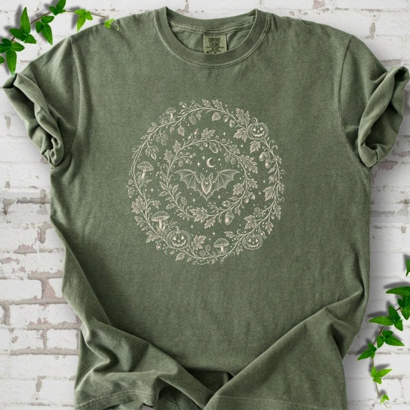 Moss Comfort Colors® T-shirt with cream botanical autumn wreath graphic featuring mushrooms, pumpkins, a bat and crescent moon