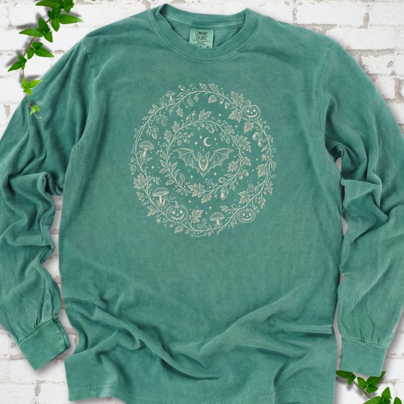Light Green Comfort Colors® long sleeve T-shirt with cream botanical autumn wreath graphic featuring mushrooms, pumpkins, a bat and crescent moon
