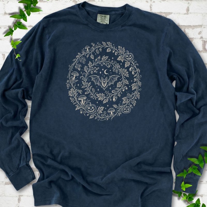 Midnight Comfort Colors® long sleeve T-shirt with cream botanical autumn wreath graphic featuring mushrooms, pumpkins, a bat and crescent moon