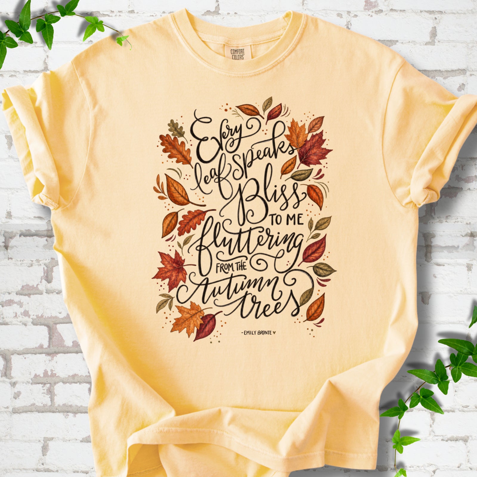 Butter Comfort Colors® T-shirt flat lay with the Every Leaf Speaks Bliss Emily Brontë quote and autumn leaves.