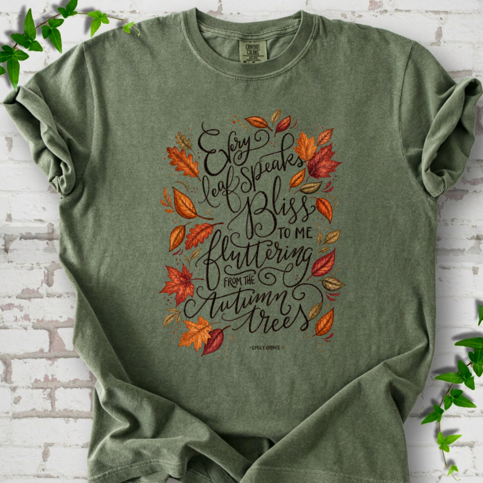 Moss Comfort Colors® T-shirt flat lay with the Every Leaf Speaks Bliss Emily Brontë quote and autumn leaves.