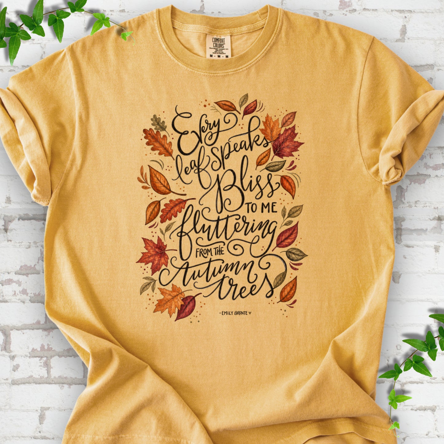 Mustard Comfort Colors® T-shirt flat lay with the Every Leaf Speaks Bliss Emily Brontë quote and autumn leaves.
