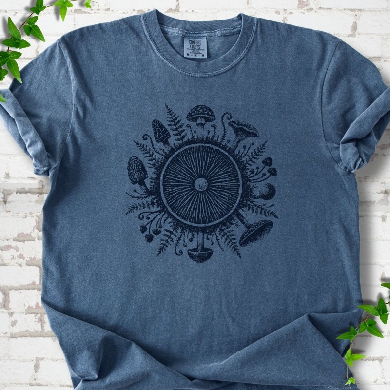Denim blue short-sleeve tee with a mushroom gill circle ringed by ferns, morels and mushrooms in navy ink.