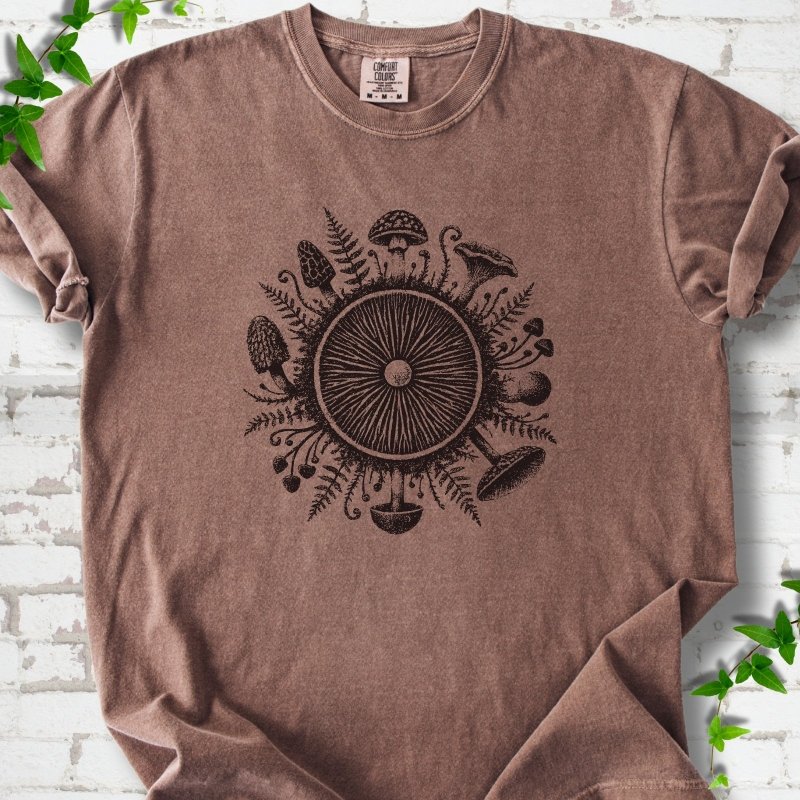 Espresso brown short-sleeve tee with a mushroom gill circle ringed by ferns, morels and mushrooms in dark brown ink.