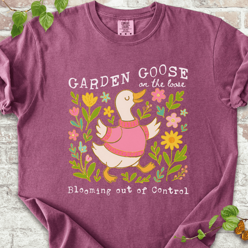 Silly gardening goose graphic on a berry Comfort Colors™ T-shirt with a flower-loving goose in full bloom.