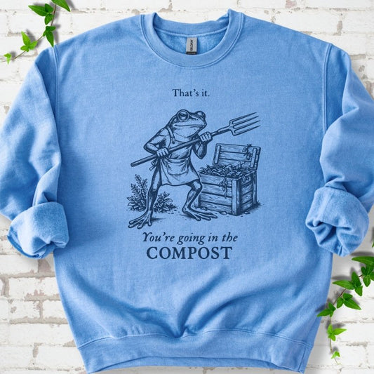 Carolina Blue classic sweatshirt laid flat, showing a frog holding a garden fork beside a compost bin and the words “That’s it. You’re going in the COMPOST.”