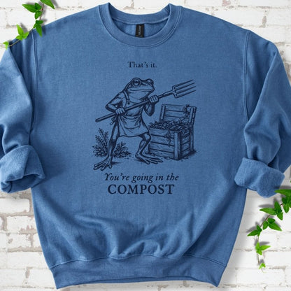 Indigo classic sweatshirt laid flat, showing a frog holding a garden fork beside a compost bin and the words “That’s it. You’re going in the COMPOST.”