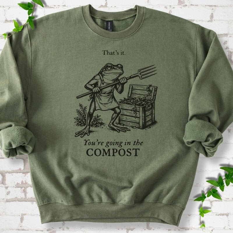 Military Green classic sweatshirt laid flat, showing a frog holding a garden fork beside a compost bin and the words “That’s it. You’re going in the COMPOST.”