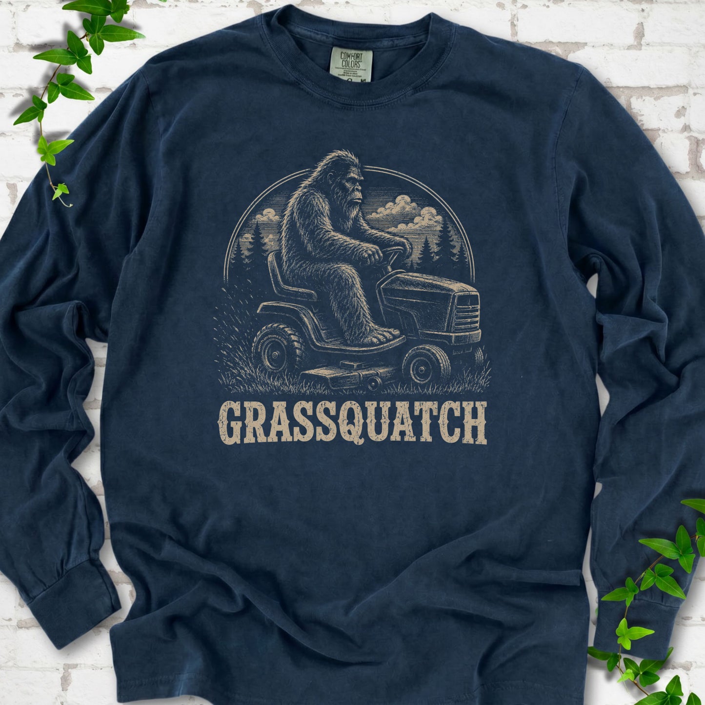 Midnight Comfort Colors® long sleeve T-shirt front mockup featuring Bigfoot riding a lawn mower above the word Grassquatch.