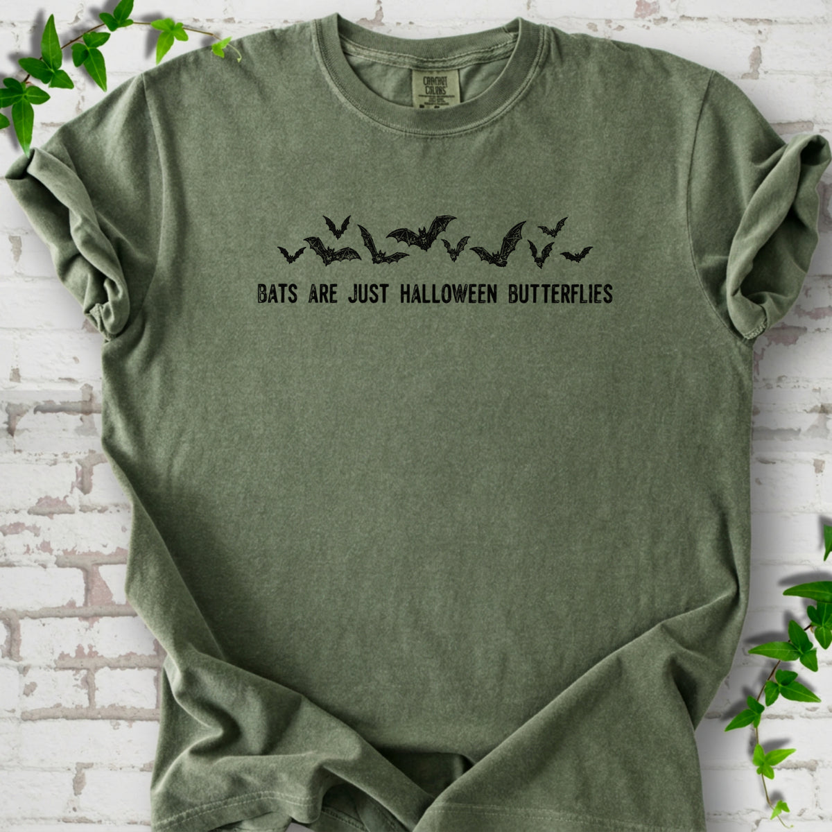 Moss Comfort Colors® T-shirt flat lay with black flying bats and “Bats Are Just Halloween Butterflies” lettering.