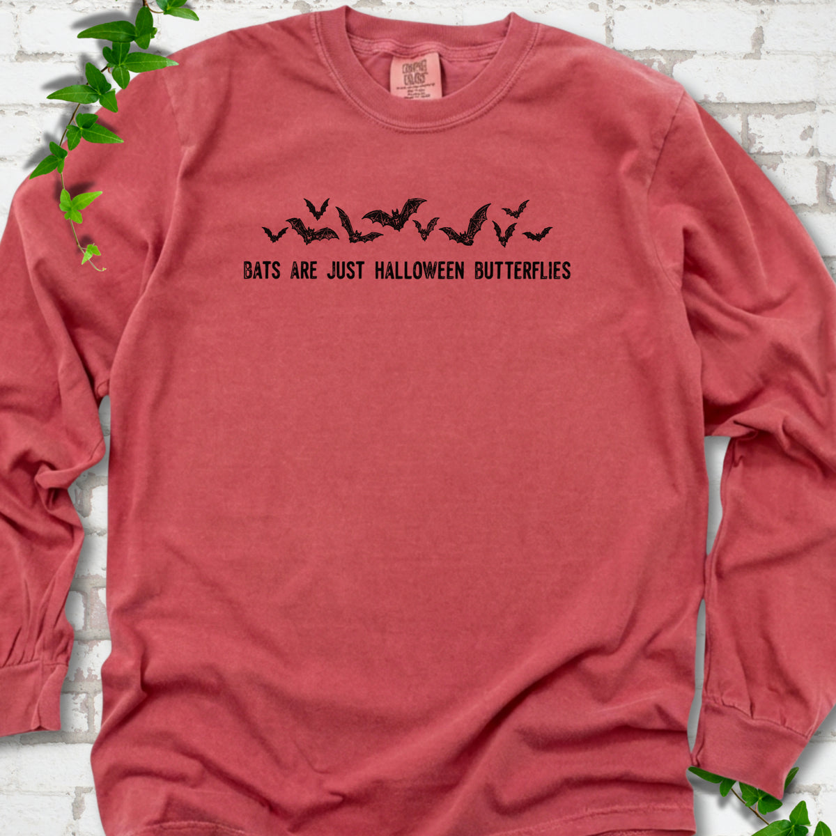 Crimson Comfort Colors® long sleeve tee flat lay with black flying bats and “Bats Are Just Halloween Butterflies” lettering.