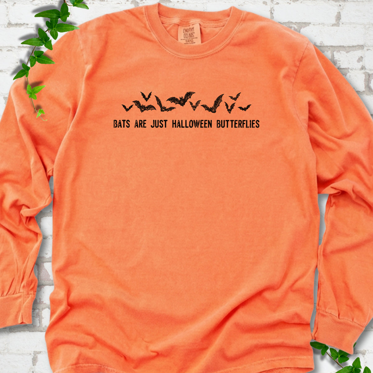 Melon Comfort Colors® long sleeve tee flat lay with black flying bats and “Bats Are Just Halloween Butterflies” lettering.