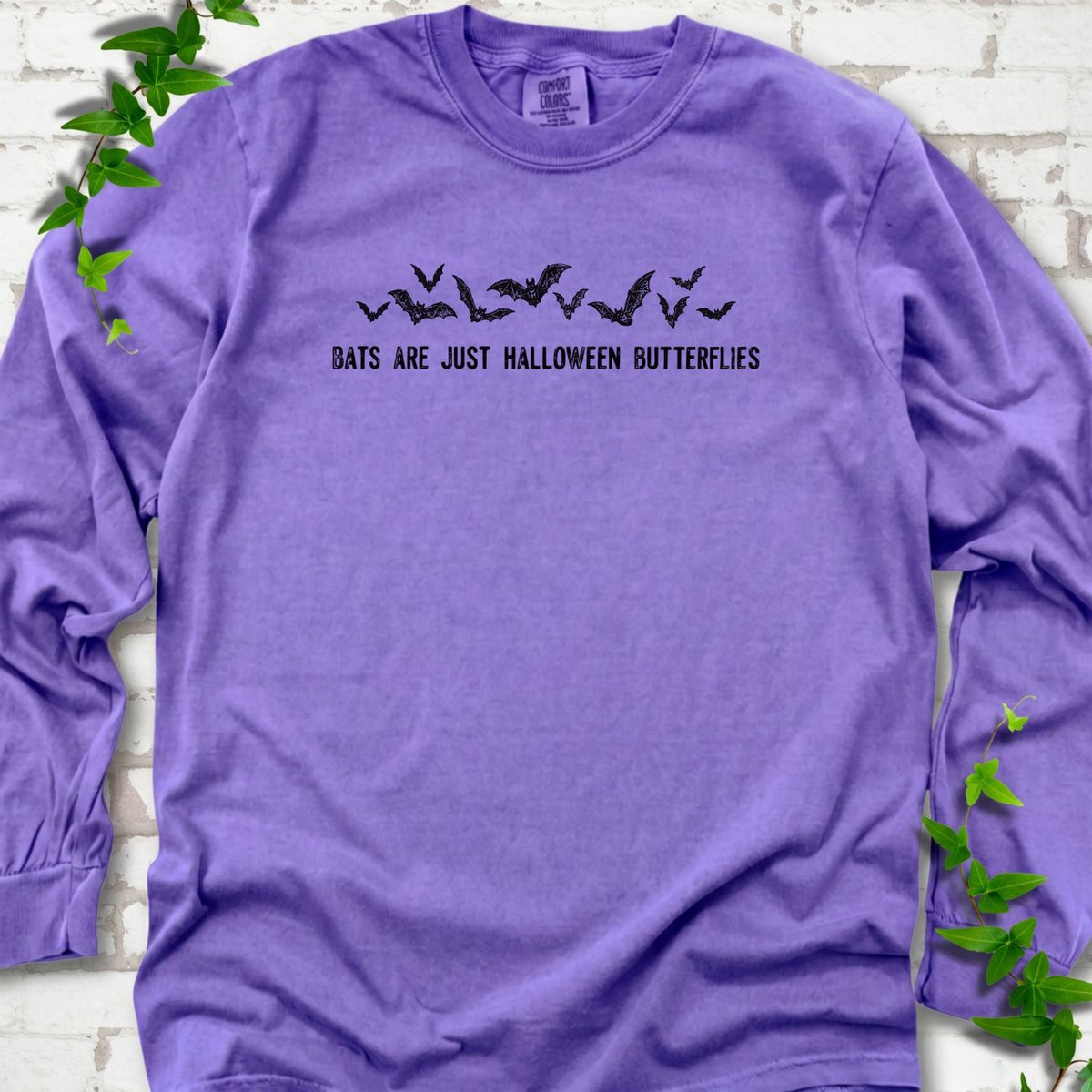 Violet Comfort Colors® long sleeve tee flat lay with black flying bats and “Bats Are Just Halloween Butterflies” lettering.