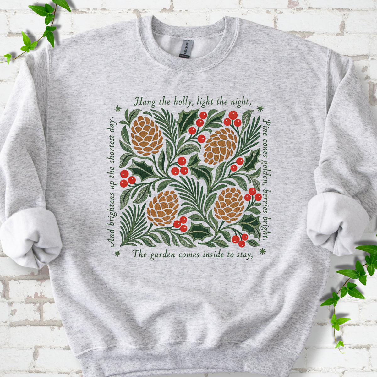 Ash classic sweatshirt shown flat with green holly, red berries, pine cones and the "Hang the Holly" seasonal verse
