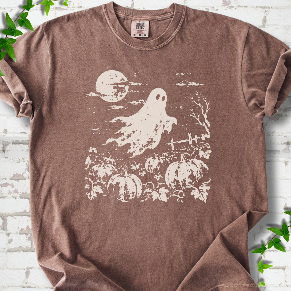 Espresso Comfort Colors® T-shirt flat lay featuring a distressed ghost floating above a pumpkin patch beneath a full moon.