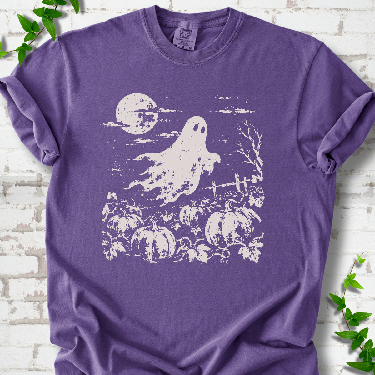 Grape Comfort Colors® T-shirt flat lay featuring a distressed ghost floating above a pumpkin patch beneath a full moon.