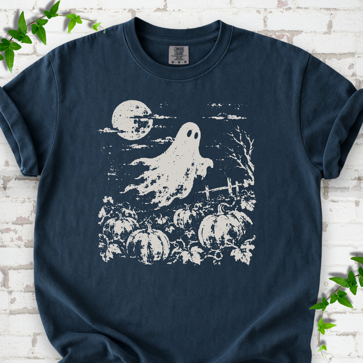 Midnight Comfort Colors® T-shirt flat lay featuring a distressed ghost floating above a pumpkin patch beneath a full moon.