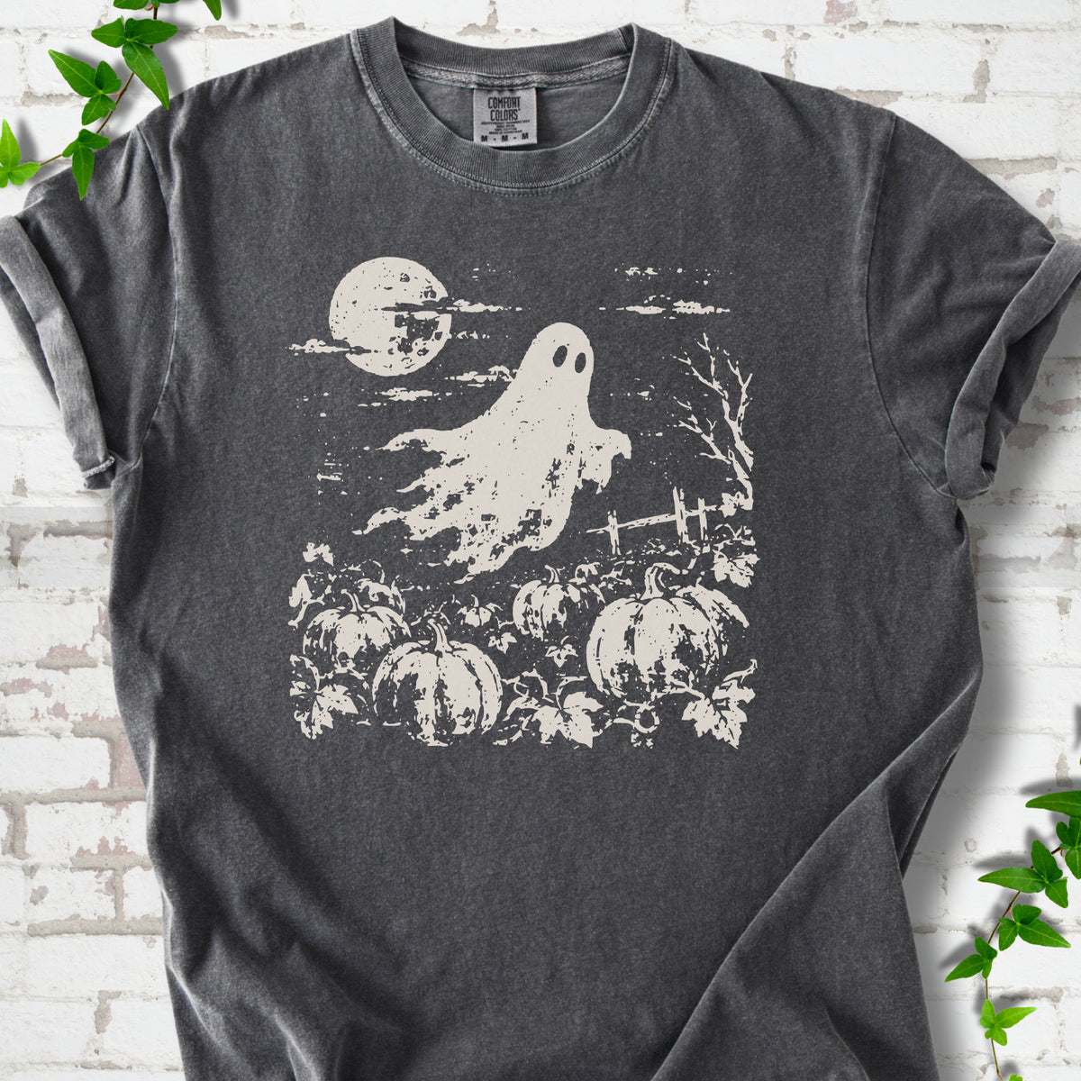 Pepper Comfort Colors® T-shirt flat lay featuring a distressed ghost floating above a pumpkin patch beneath a full moon.