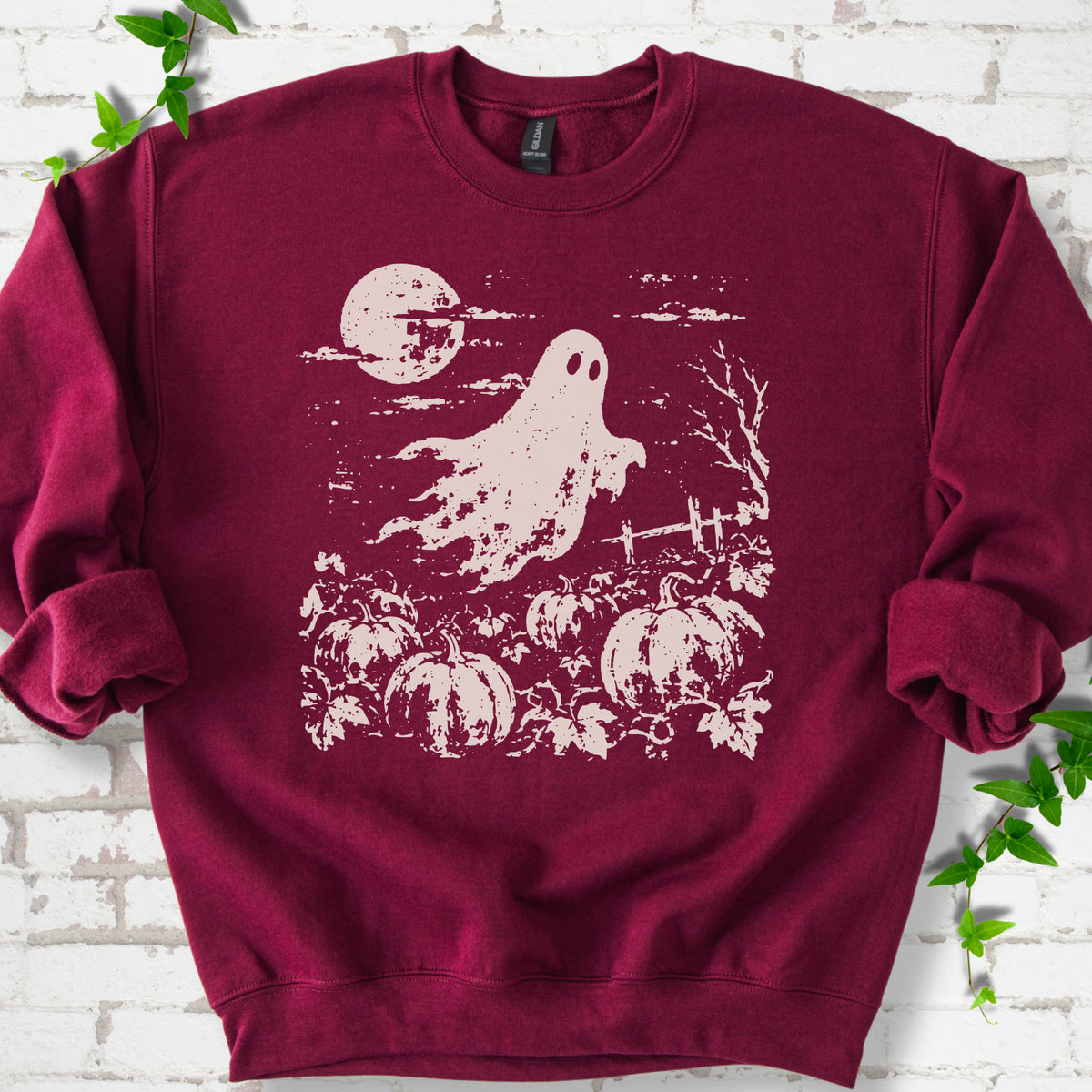Maroon crewneck sweatshirt flat lay featuring a distressed ghost floating above a pumpkin patch beneath a full moon.