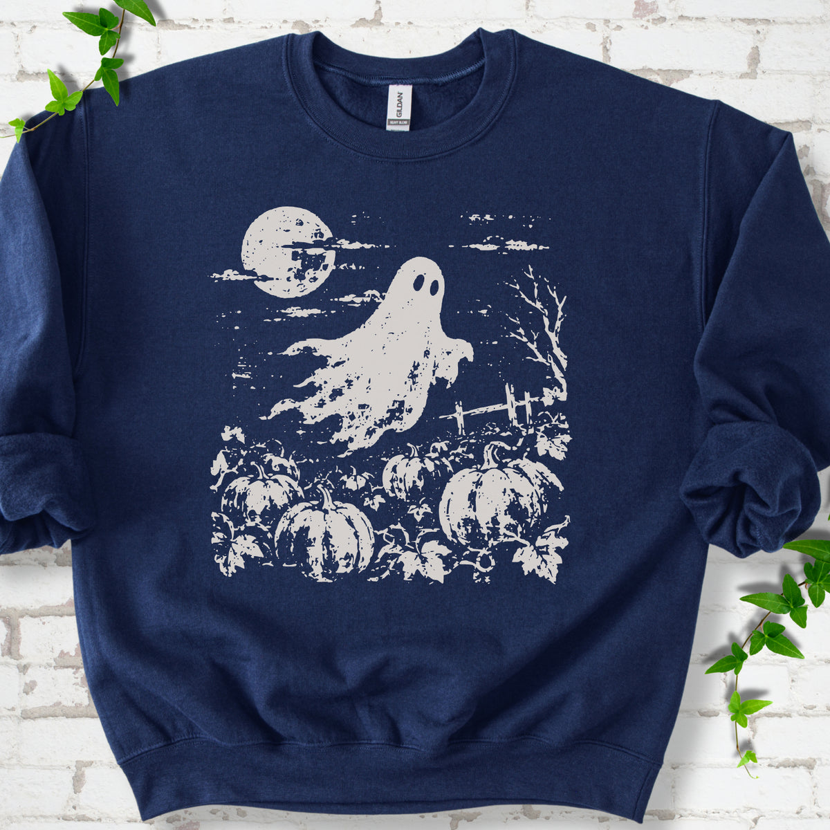 Navy crewneck sweatshirt flat lay featuring a distressed ghost floating above a pumpkin patch beneath a full moon.