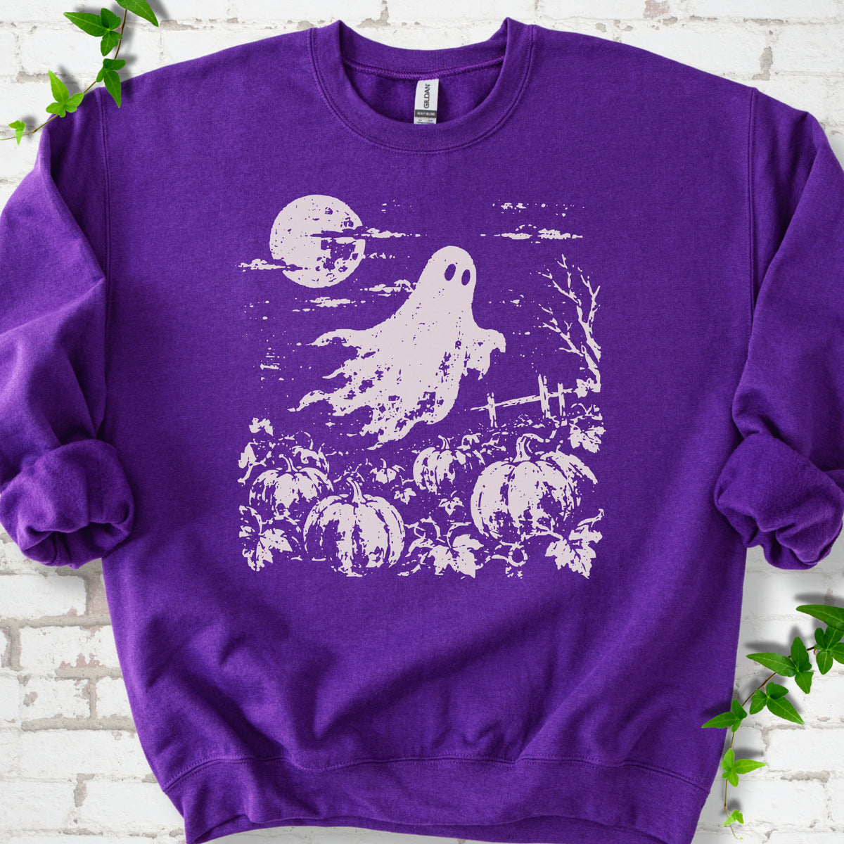 Purple crewneck sweatshirt flat lay featuring a distressed ghost floating above a pumpkin patch beneath a full moon.