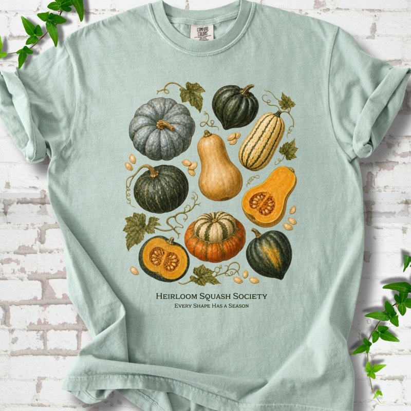 Bay Comfort Colors® short sleeve T-shirt flat lay featuring an illustrated collection of heirloom squash, pumpkins, seeds and vines with text "Heirloom Squash Society" and "Every shape has a season"