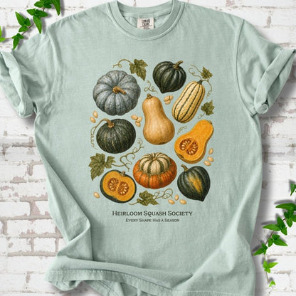 Bay Comfort Colors® short sleeve T-shirt flat lay featuring an illustrated collection of heirloom squash, pumpkins, seeds and vines with text "Heirloom Squash Society" and "Every shape has a season"